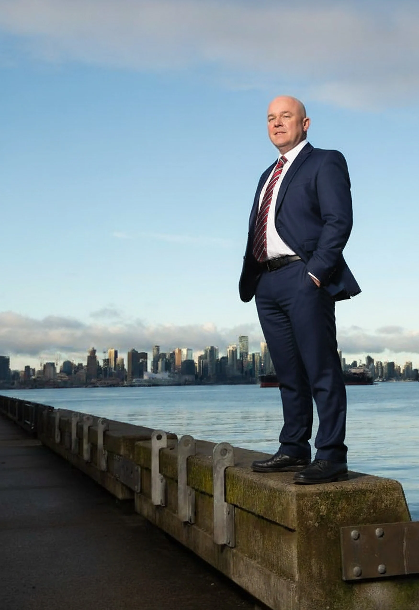 Rick Colbourne standing on a pier on the North Shore with the Vancouver skyline behind