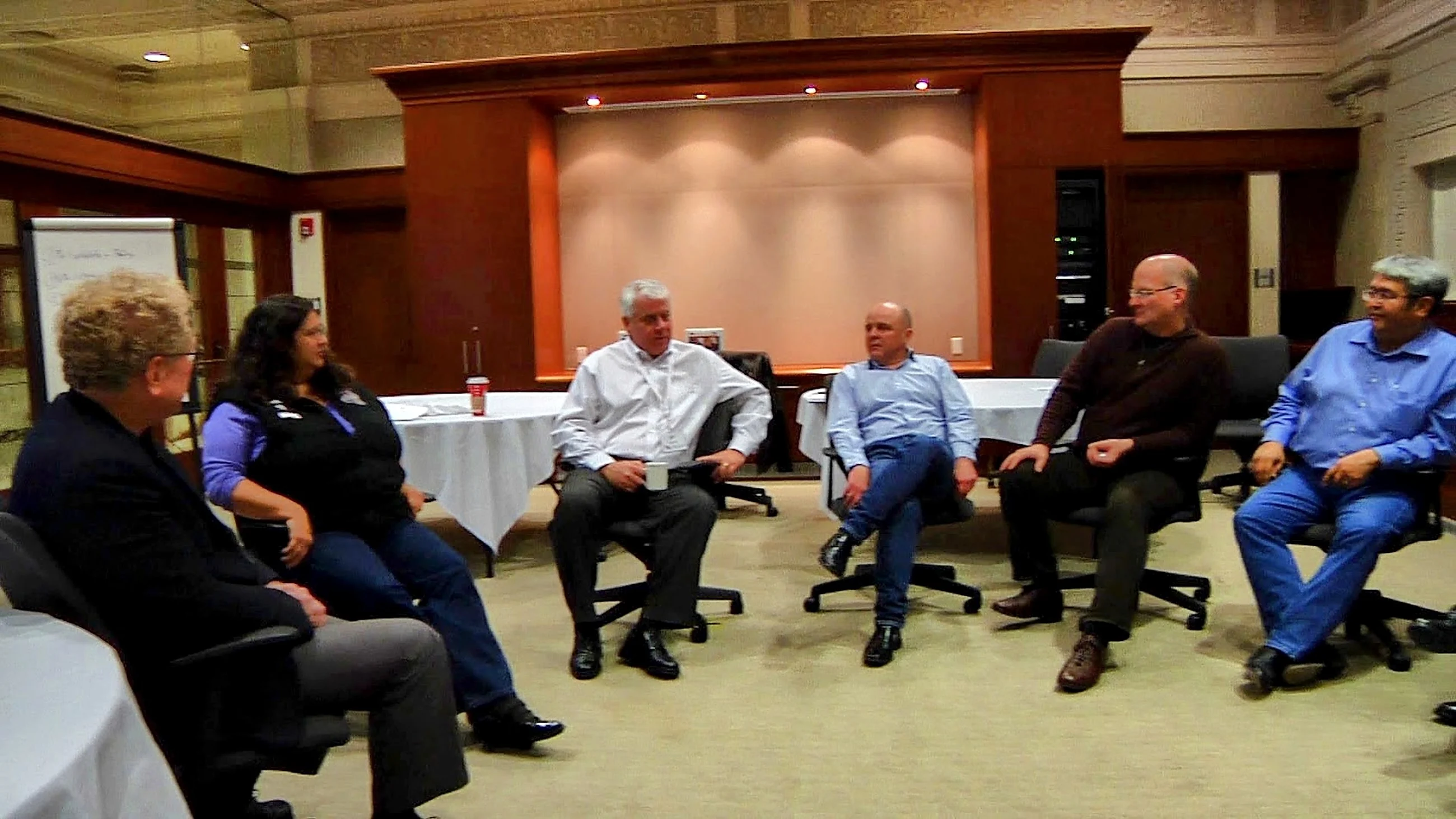 A circle of chairs in a panelled room, participants in discussion