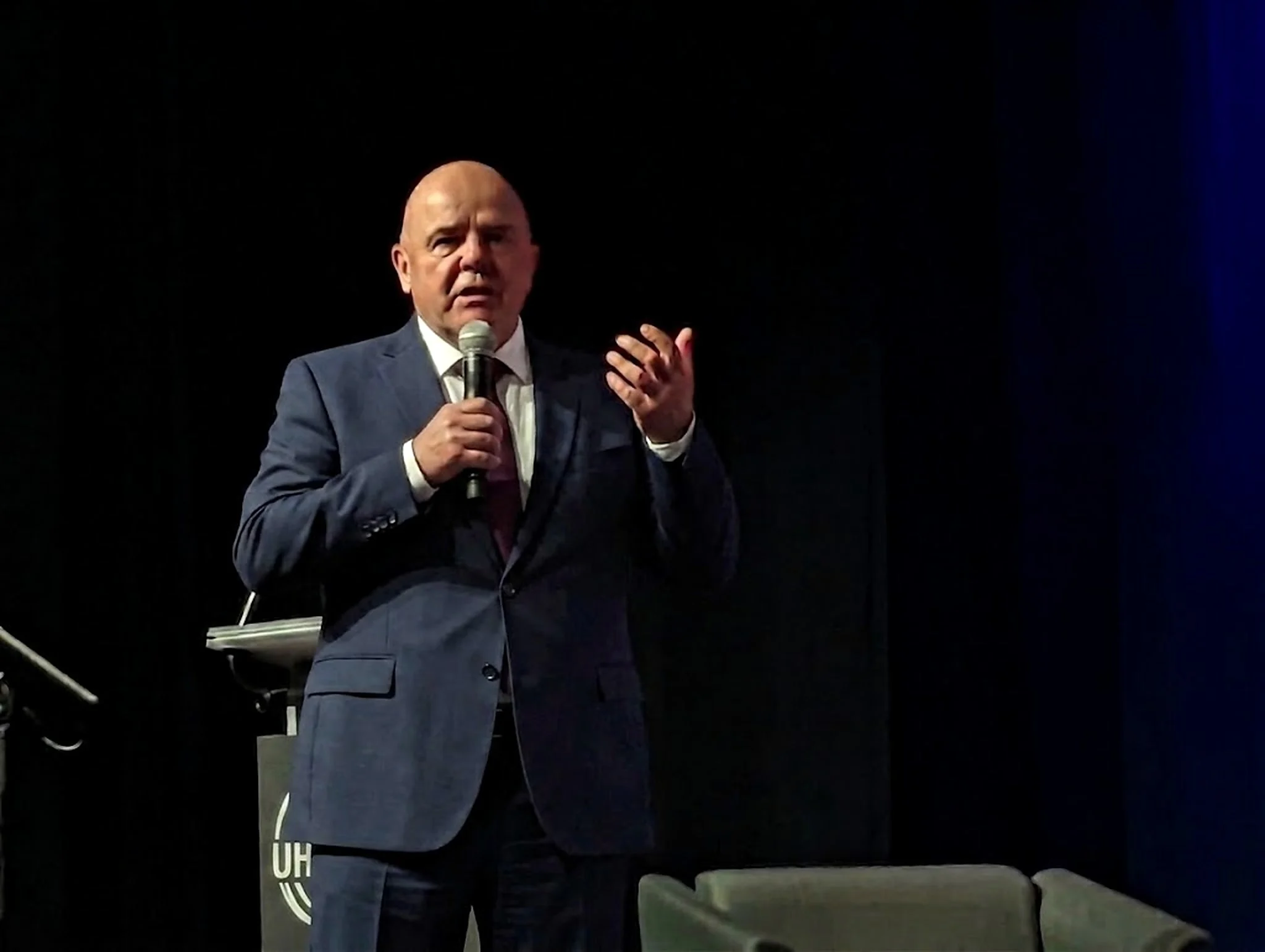 Rick Colbourne speaking on stage, microphone in hand, mid-gesture