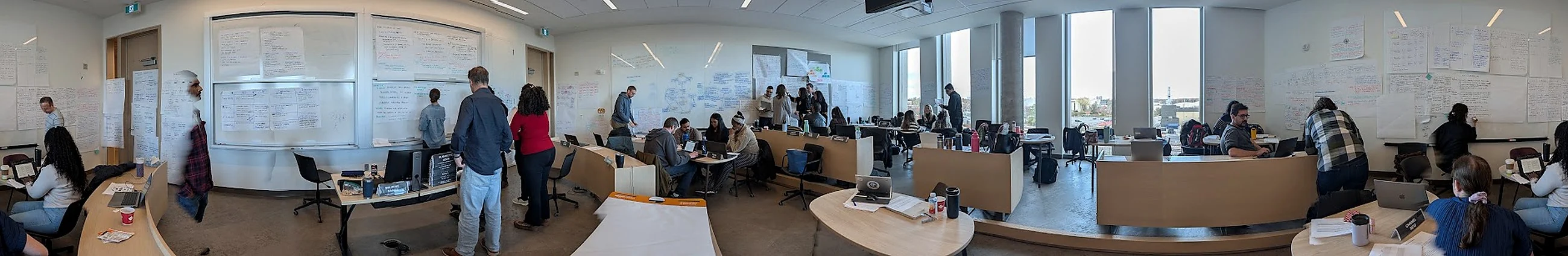 A studio room with every wall covered in working paper, participants at tables and standing at the walls