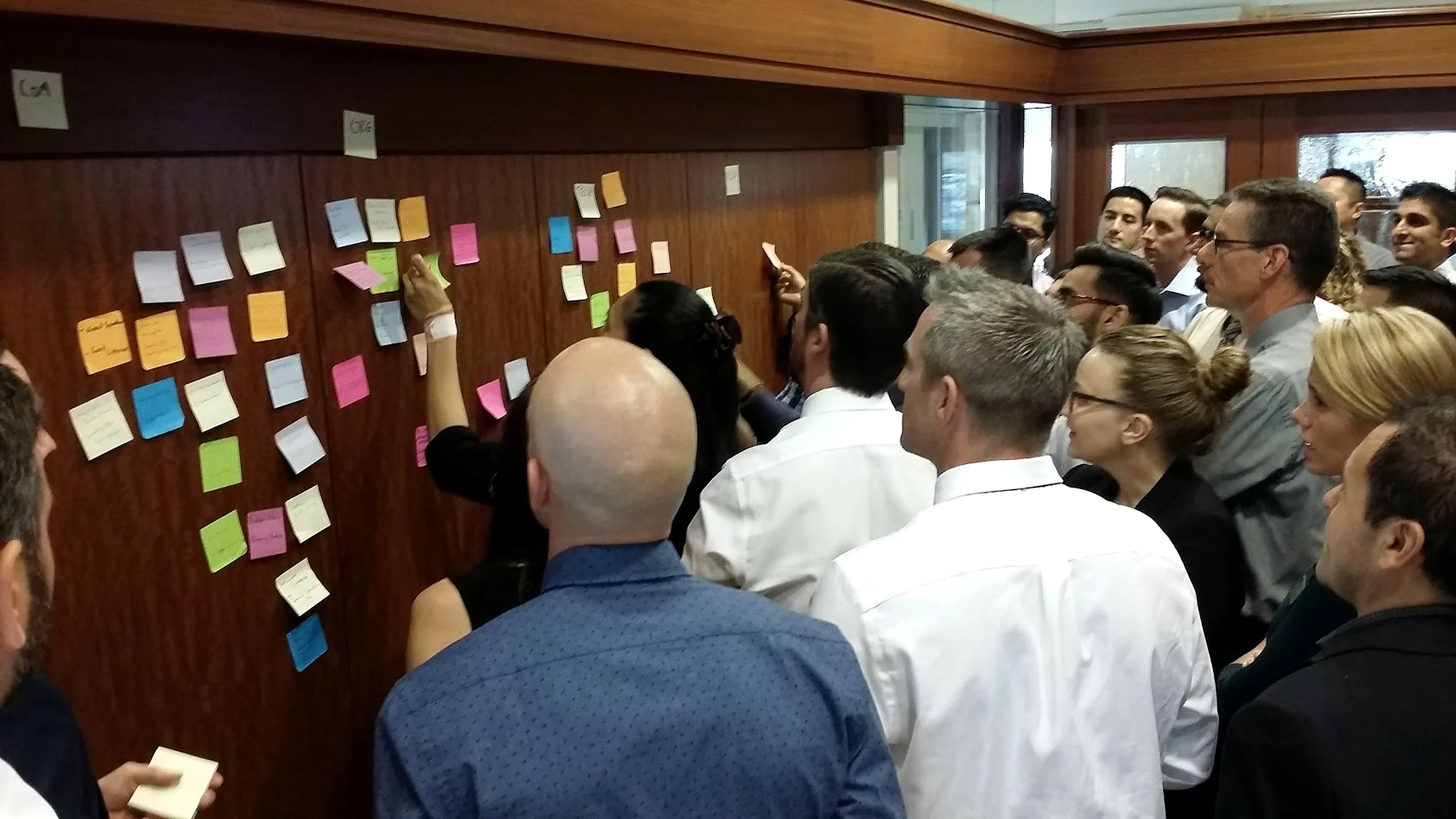 A group at a wall of written notes, one participant placing a card, others reading and discussing